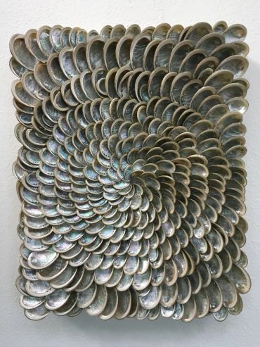 Art piece with shells arranged in a spiral pattern on a square base.