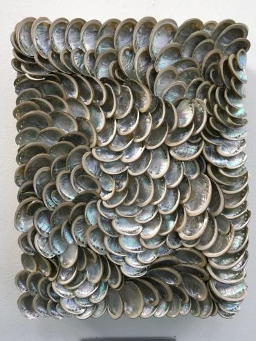 A textured art piece made of overlapping iridescent shells arranged in swirling patterns.