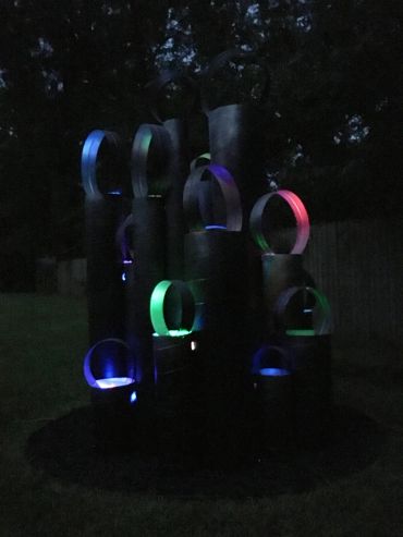 Dark outdoor sculpture illuminated with colorful LED rings.