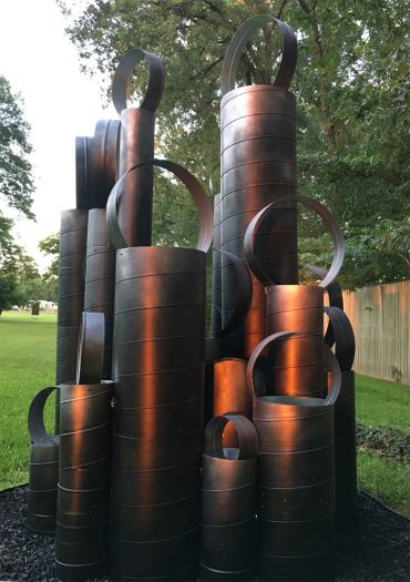 Tall cylindrical metal sculptures with circular handles arranged outdoors.