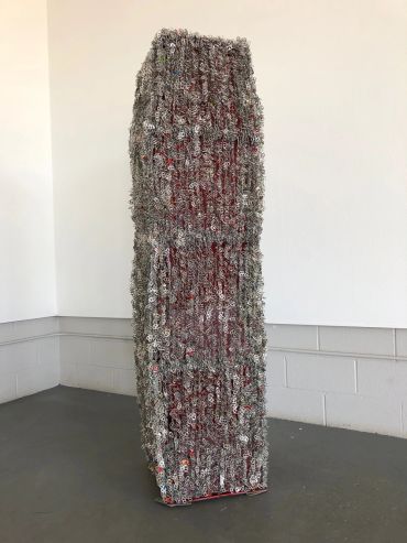 Tall sculpture made of densely packed metal bottle caps.
