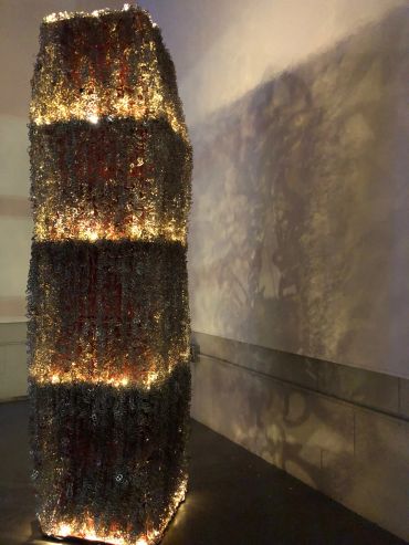 Tall illuminated sculpture casting intricate shadows on a wall.