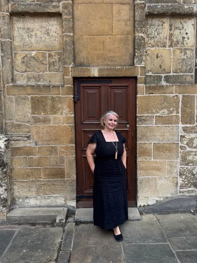 Woman in black dress standing by old wooden door.
