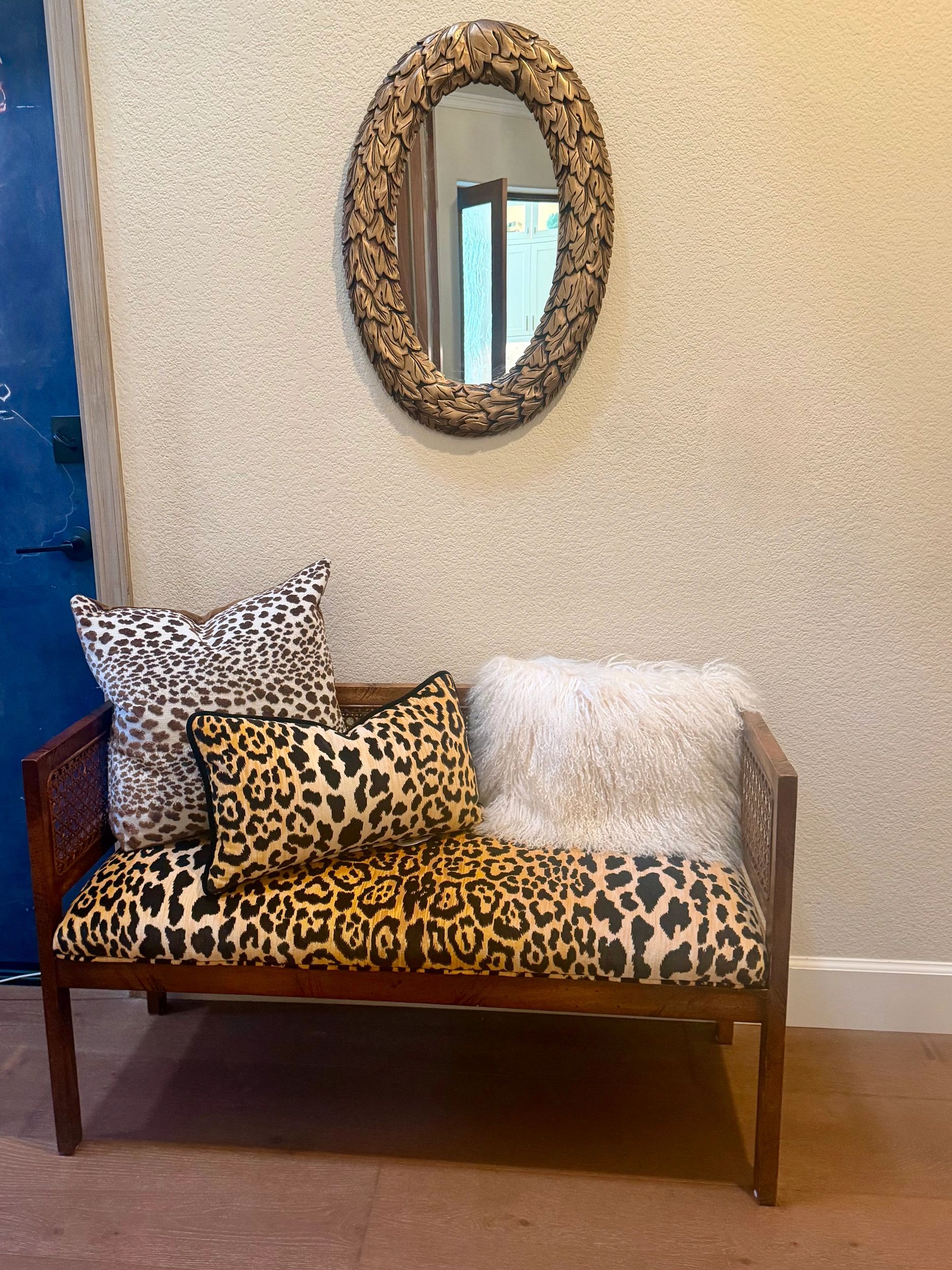 Cozy bench with animal print cushions and a leafy framed mirror.