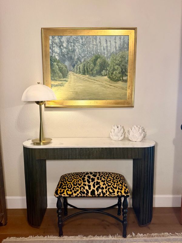 Stylish console table setup with lamp, painting, and patterned stool.