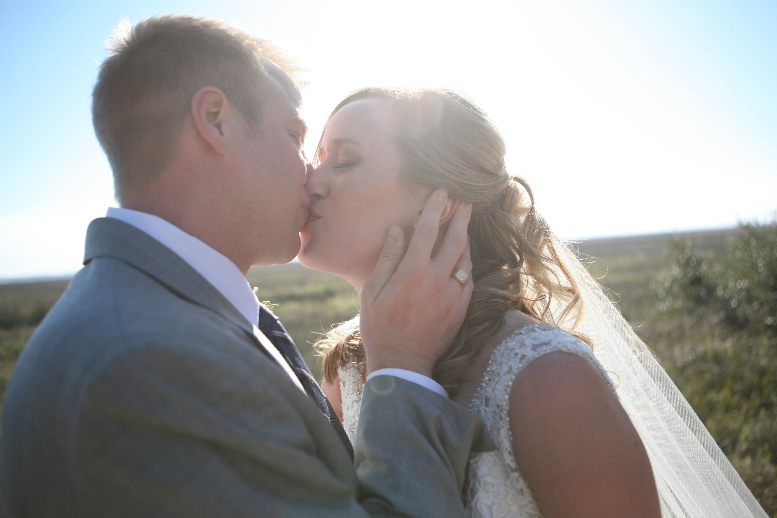 Bride and groom sharing a kiss with sunlight behind them.
