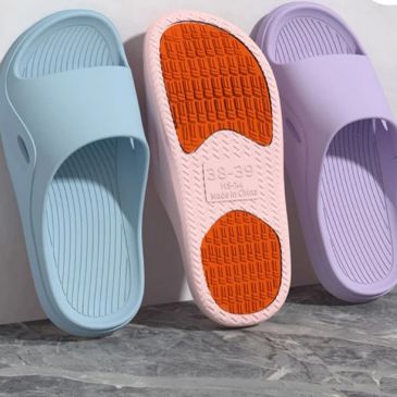 Three colorful slip-on sandals with textured soles displayed against a wall.