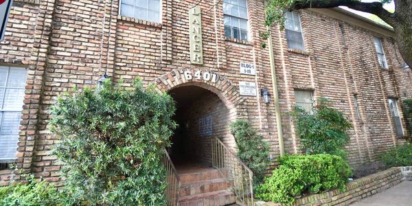 Brick apartment building entrance with greenery and staircase.