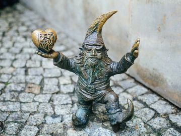 A small bronze gnome statue holding a heart stands on cobblestone pavement.