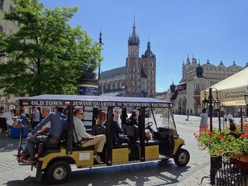 Tourists ride an open tram in a historic European city square.