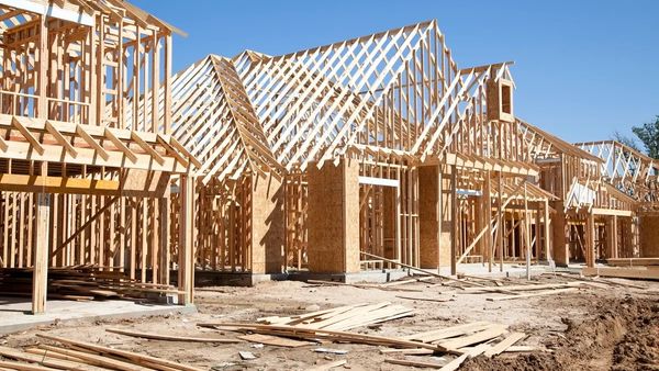 Wooden frames of houses under construction against a clear blue sky.