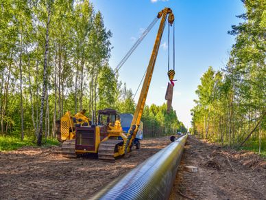 Yellow crane lifting pipeline segment in forest clearing.