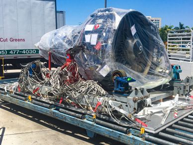 Wrapped airplane engine on a blue transport pallet at an outdoor facility.