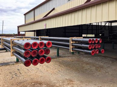 Stacks of industrial pipes with red ends stored outside a warehouse.