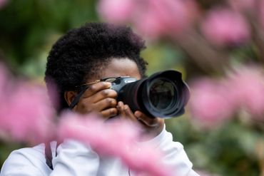 A photographer capturing images through pink flowers with a Canon camera.