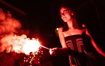 Young woman enjoying a sparkler at night, illuminated by vibrant red light.
