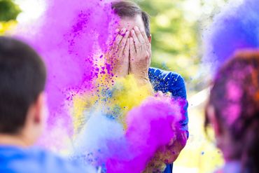 Person covering face amidst colorful powder during a celebration.