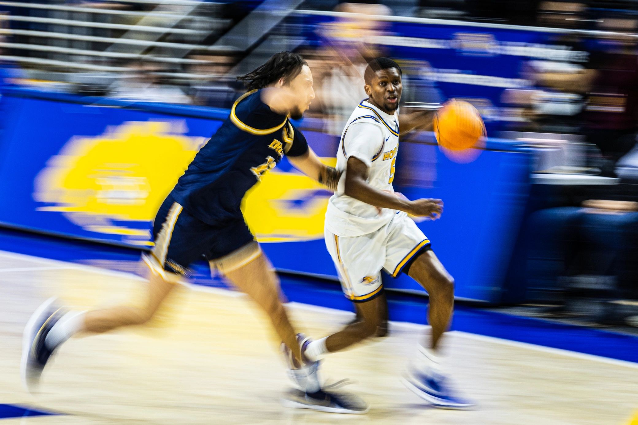 Two basketball players in motion during a game, one in white and one in blue.