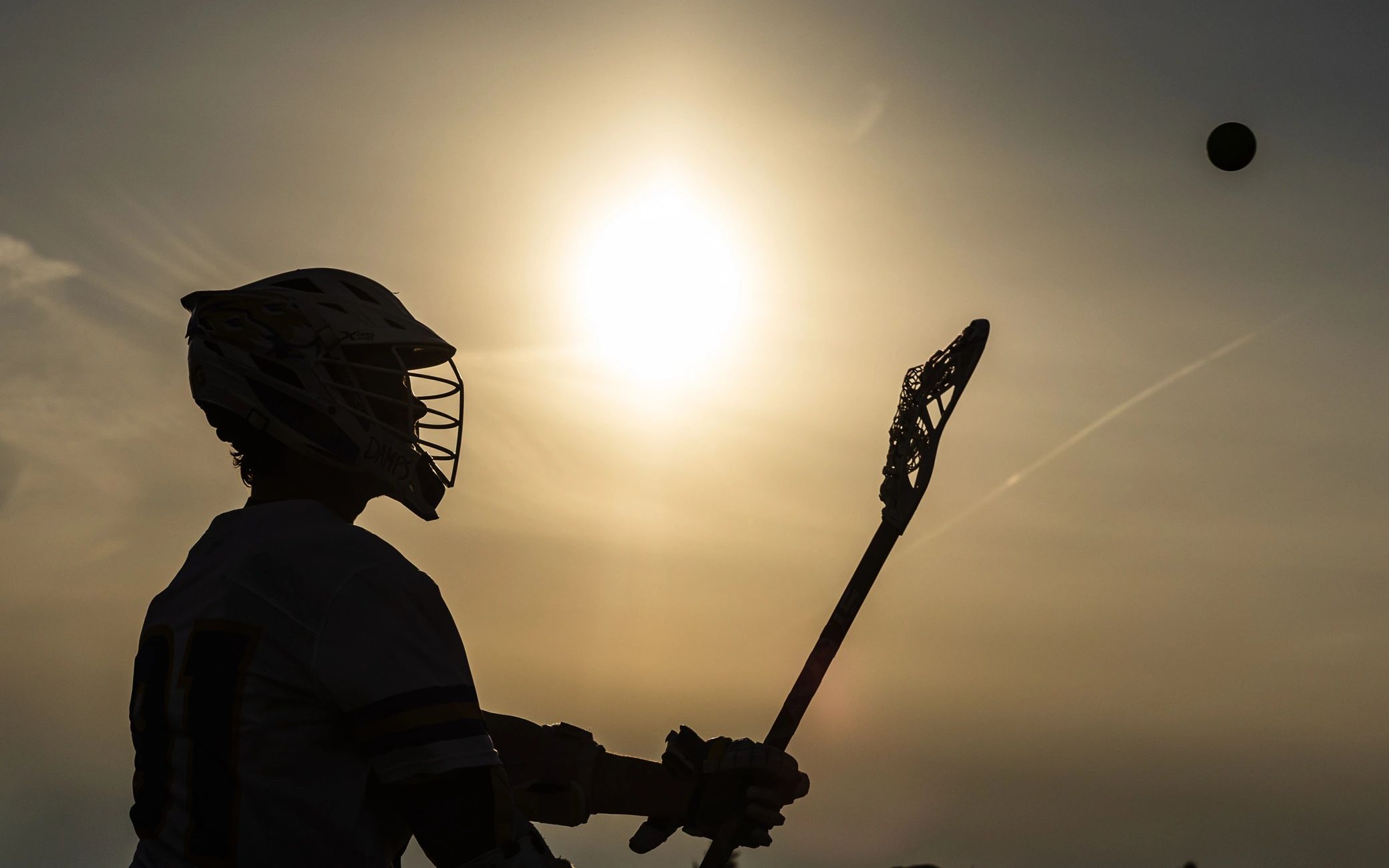Silhouette of a lacrosse player poised to catch the ball against a setting sun.