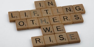 Wooden scrabble tiles that read “in lifting others we rise”