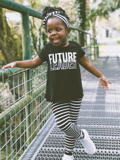 Happy very young girl of Color on bridge with a shirt that says “Future Leader”