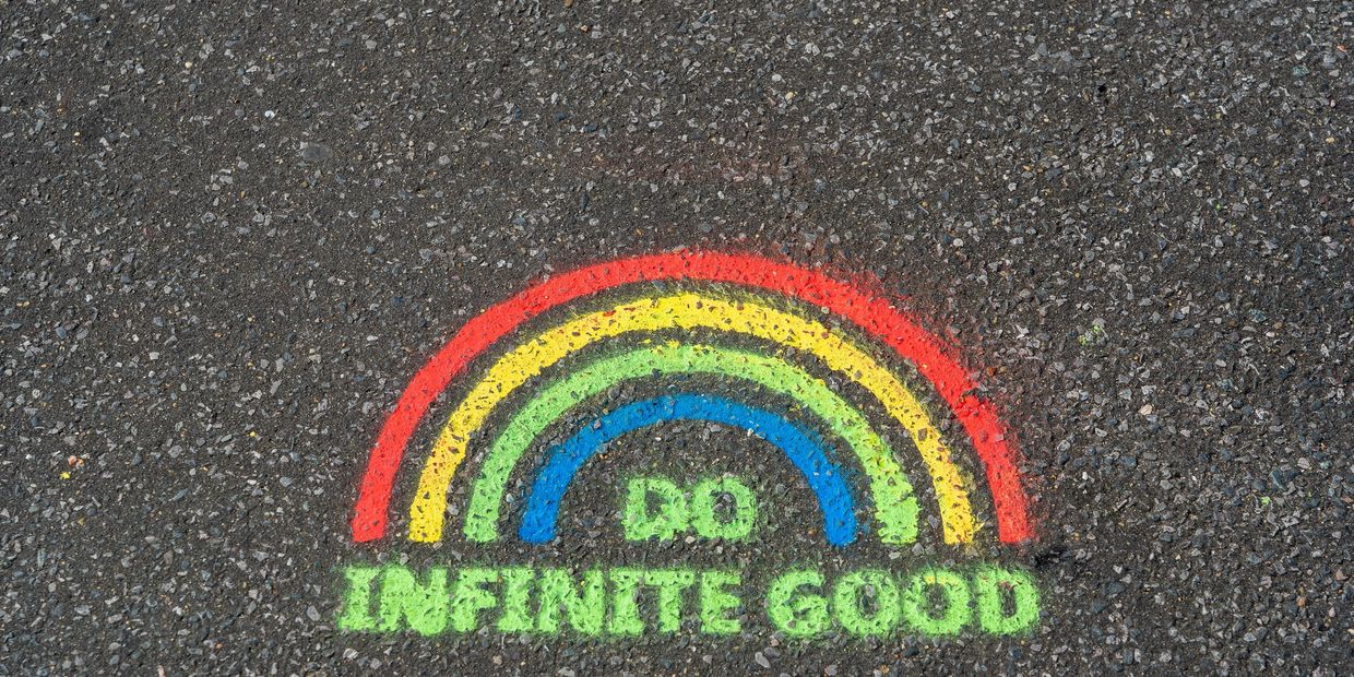 Sidewalk sign of a rainbow with the words “Do infinite good” underneath 