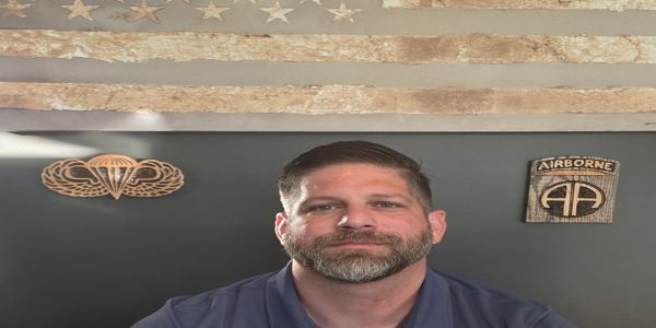 Man in front of a rustic American flag and military decor.