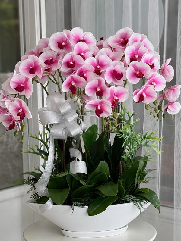 Elegant pink orchids in a white vase with a silver ribbon.