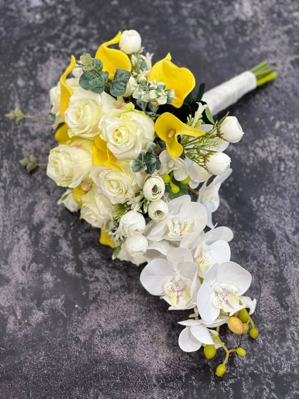 Elegant bouquet of white roses, yellow calla lilies, and white orchids on a dark textured surface.