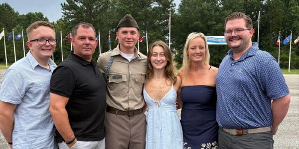 A group of six people posing outdoors with flags in the background.