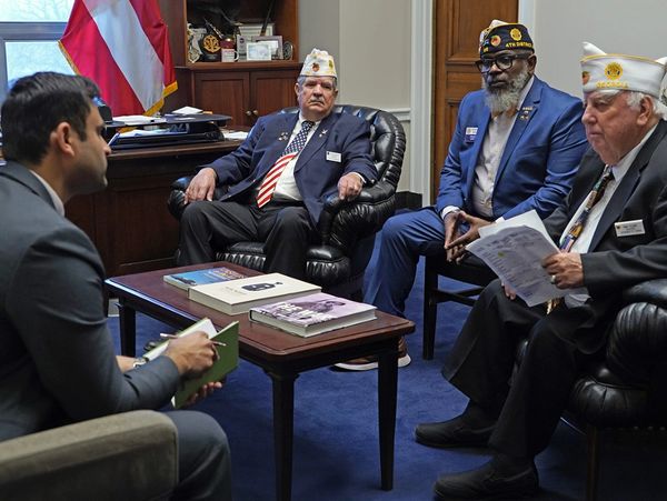 Four men in a formal office, three wearing veterans' caps.