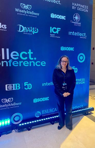 Woman standing in front of a conference backdrop with logos and event branding.