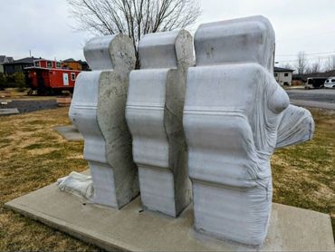 Abstract stone sculpture of three human-like figures standing side by side outdoors.