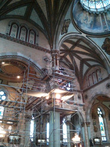 Scaffolding inside a church under restoration with vaulted ceilings and stained glass windows.