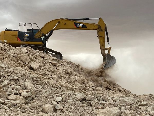 Yellow CAT excavator working on a rocky hill under a cloudy sky.