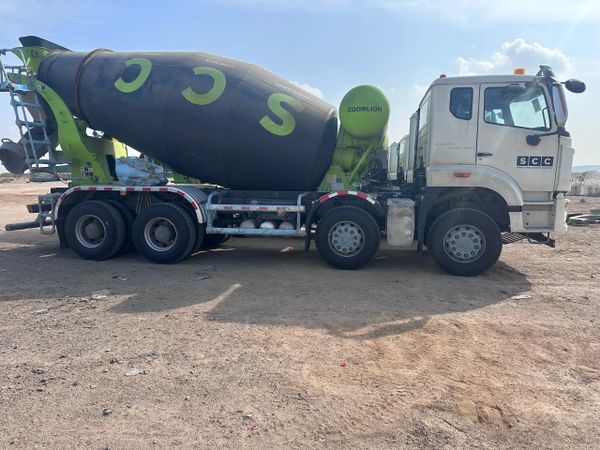 Concrete mixer truck with SCC logo parked on dirt ground under a clear sky.