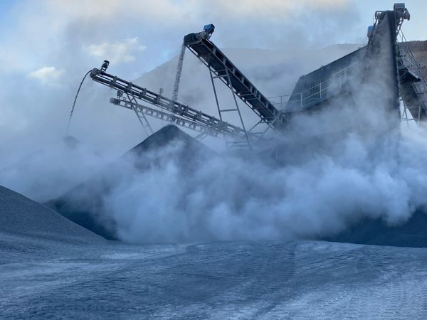 Industrial conveyors moving material amidst dense dust clouds.