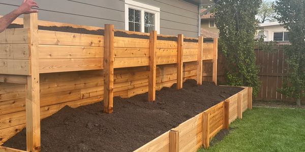 Two-tier wooden raised garden beds filled with soil in a backyard.