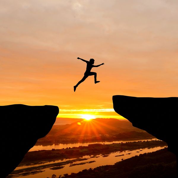 Person jumping between cliffs at sunset.