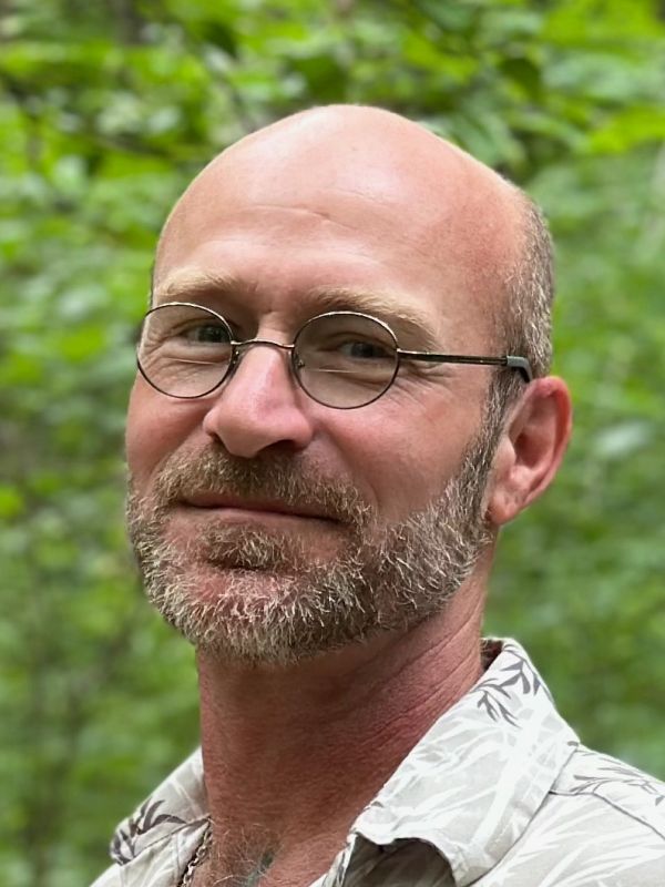 Smiling bald man with glasses outdoors.