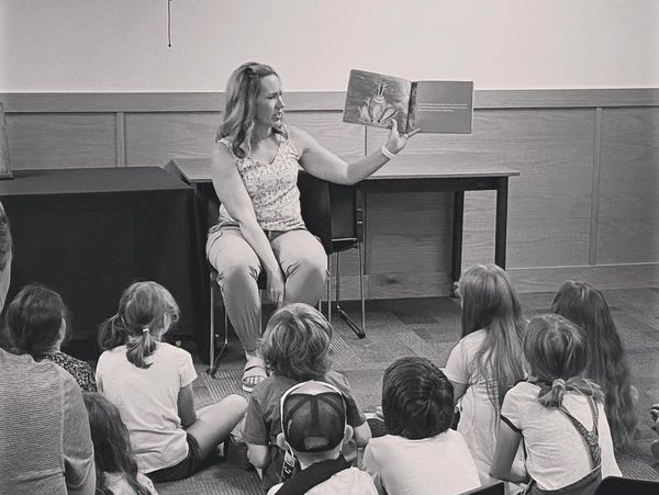 A woman reads a picture book to a group of children sitting on the floor.