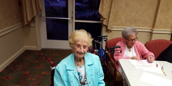 Two elderly women engaged in activities at a table in a cozy room.