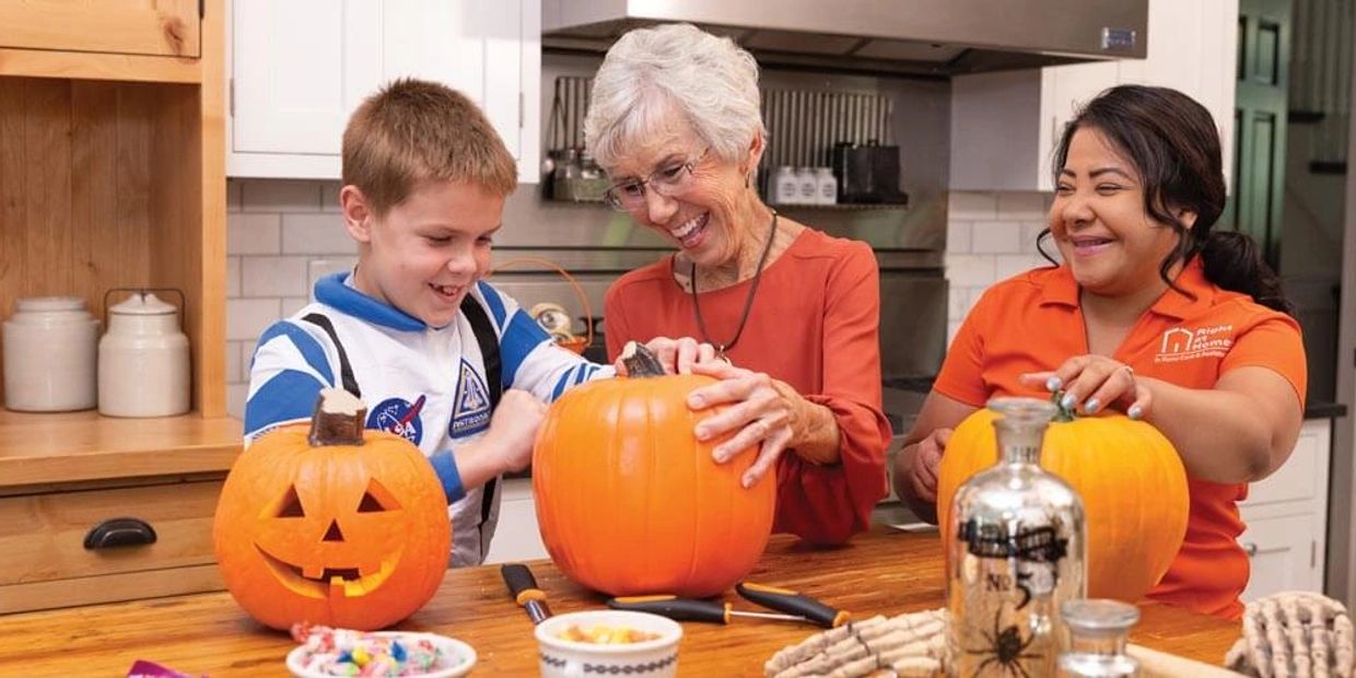 Three people carving pumpkins and smiling together.