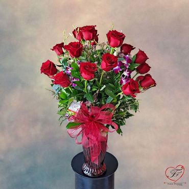 twenty four red roses arrangement with purple orchids in a glass vase.