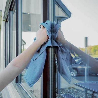 A person cleaning a glass window with a blue cloth.