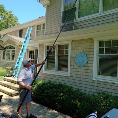 Man cleaning second-story window with a long pole.