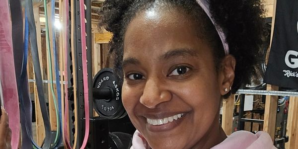 Smiling woman in a gym setting with fitness bands behind her.
