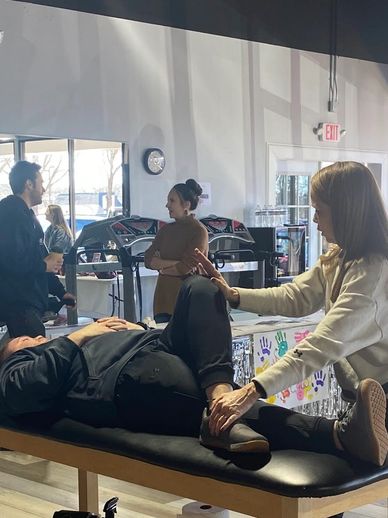 Woman stretches man's leg on a therapy table in a public space.