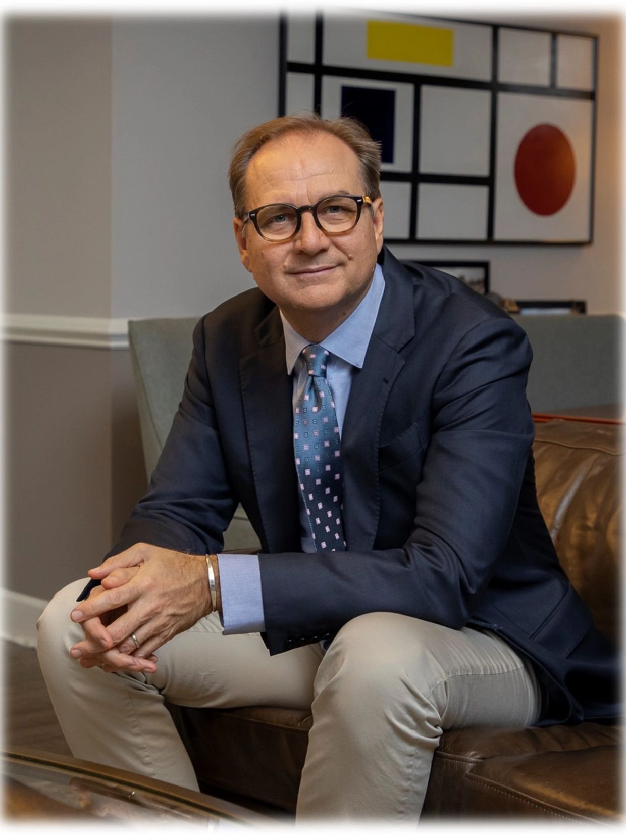 Man in a suit sitting on a leather couch with a relaxed expression.