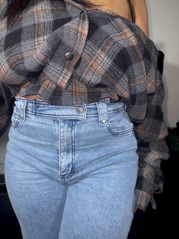Person wearing high-waisted light blue jeans and a plaid button-up shirt.